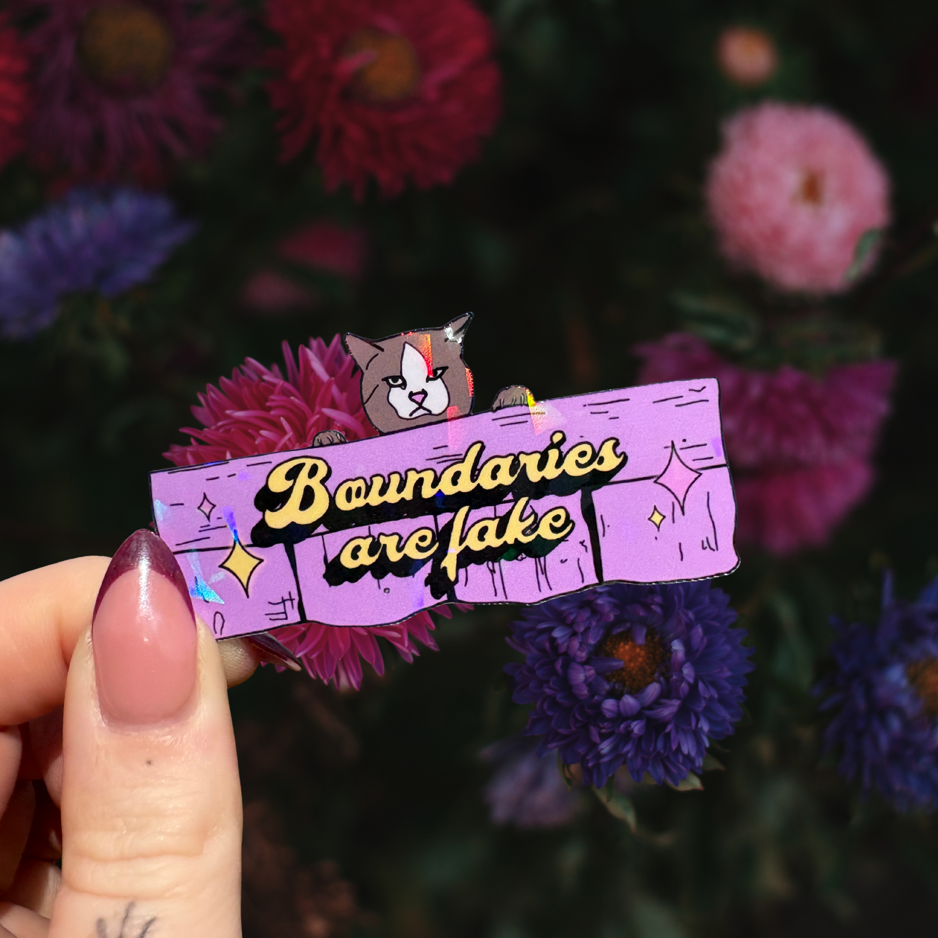 Holographic sticker of a cute/angry cat climbing a pink fence with the slogan boundaries are fake with stars.  From the neighbours from hell inspired collection perfect for water bottles, laptops, phones